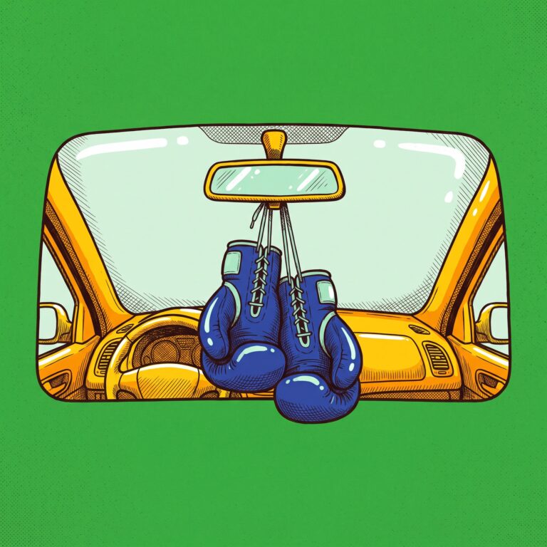 A pair of cobalt boxing gloves hanging by their laces from the rearview mirror of a yellow vehicle.